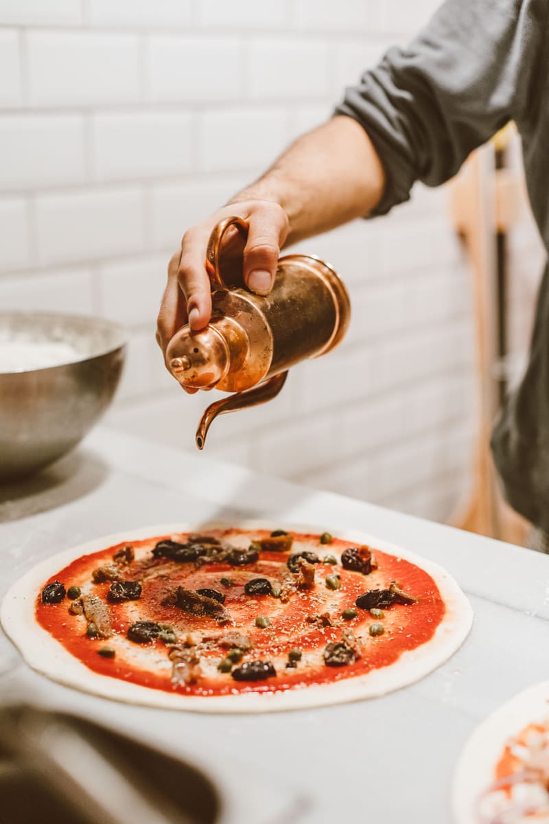 Pizzaiolo temperando uma pizza napolitana com azeite