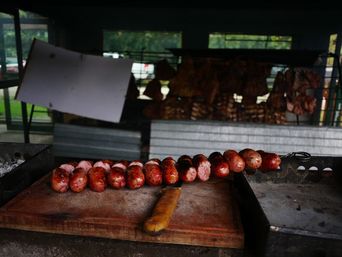 Espeto de linguiça toscana assada, inteira e em pedaços, sobre uma tábua ao lado da churrasqueira